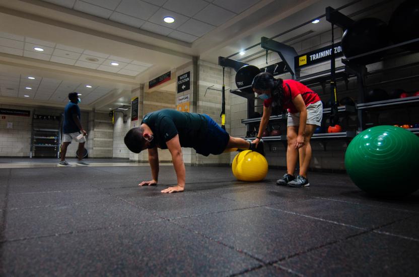 An athletic trainer instructs a student through a physio ball plank exercise.