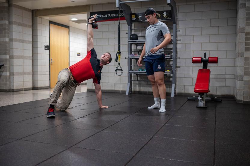 An athletic trainer demonstrates a kettle bell Turkish get up exercise in front of student.