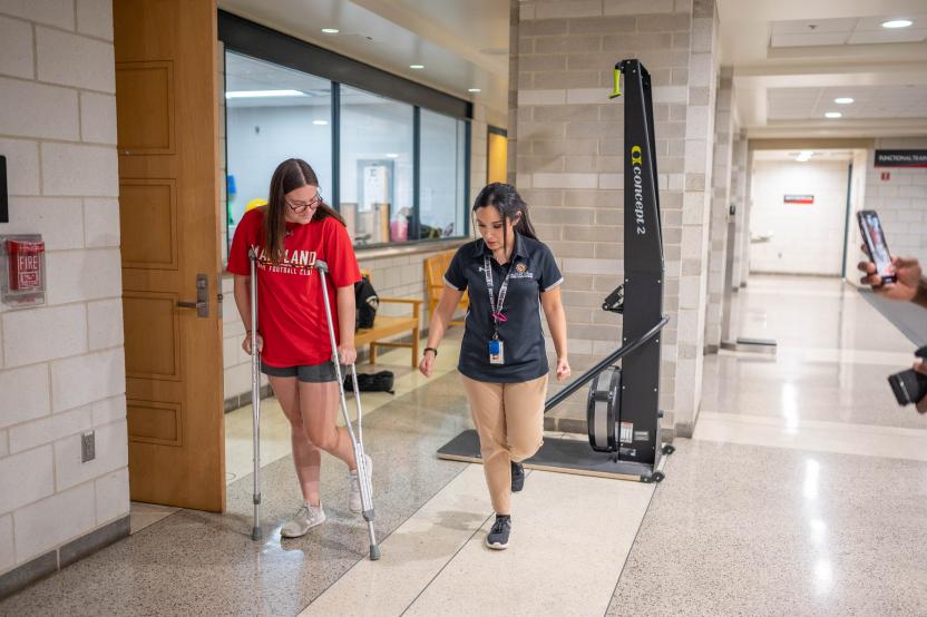 An athletic trainer walks along side a student as they are instructed how to use crutches.