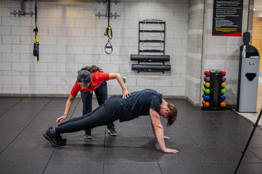 An athletic trainer instructs a student how to properly move their body through an inch worm exercise.