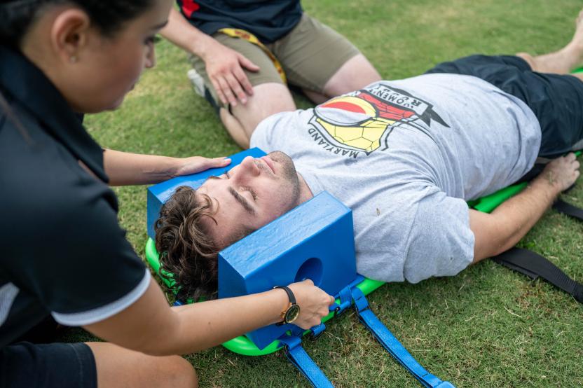 An athletic trainer stabilizes a student's head and neck while spine boarding them.