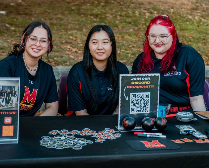 Three Terps Esports employees smile at camera, while tabling at an event.