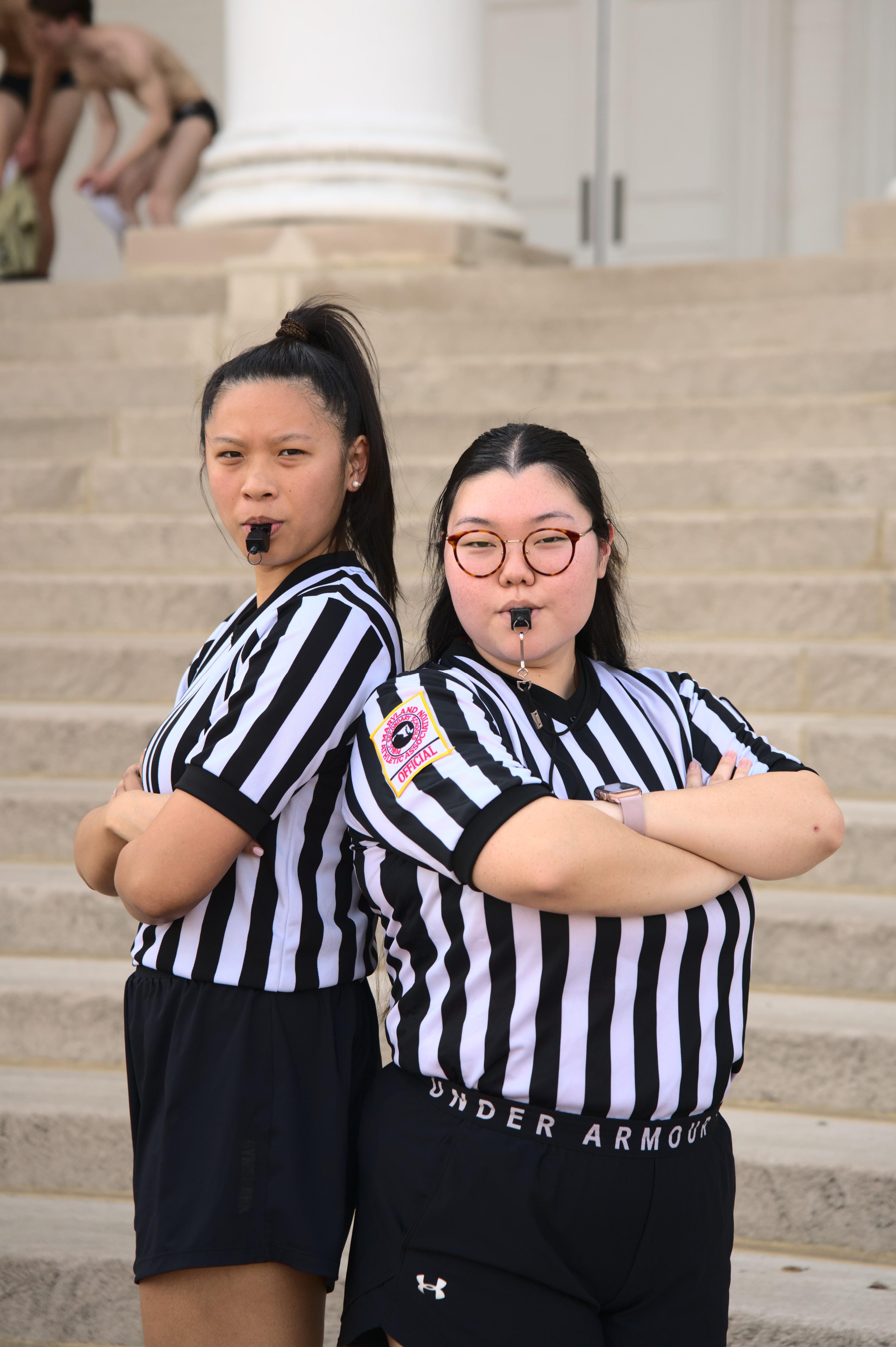two intramurals officials stand back to back with arms crossed and whistles at the ready