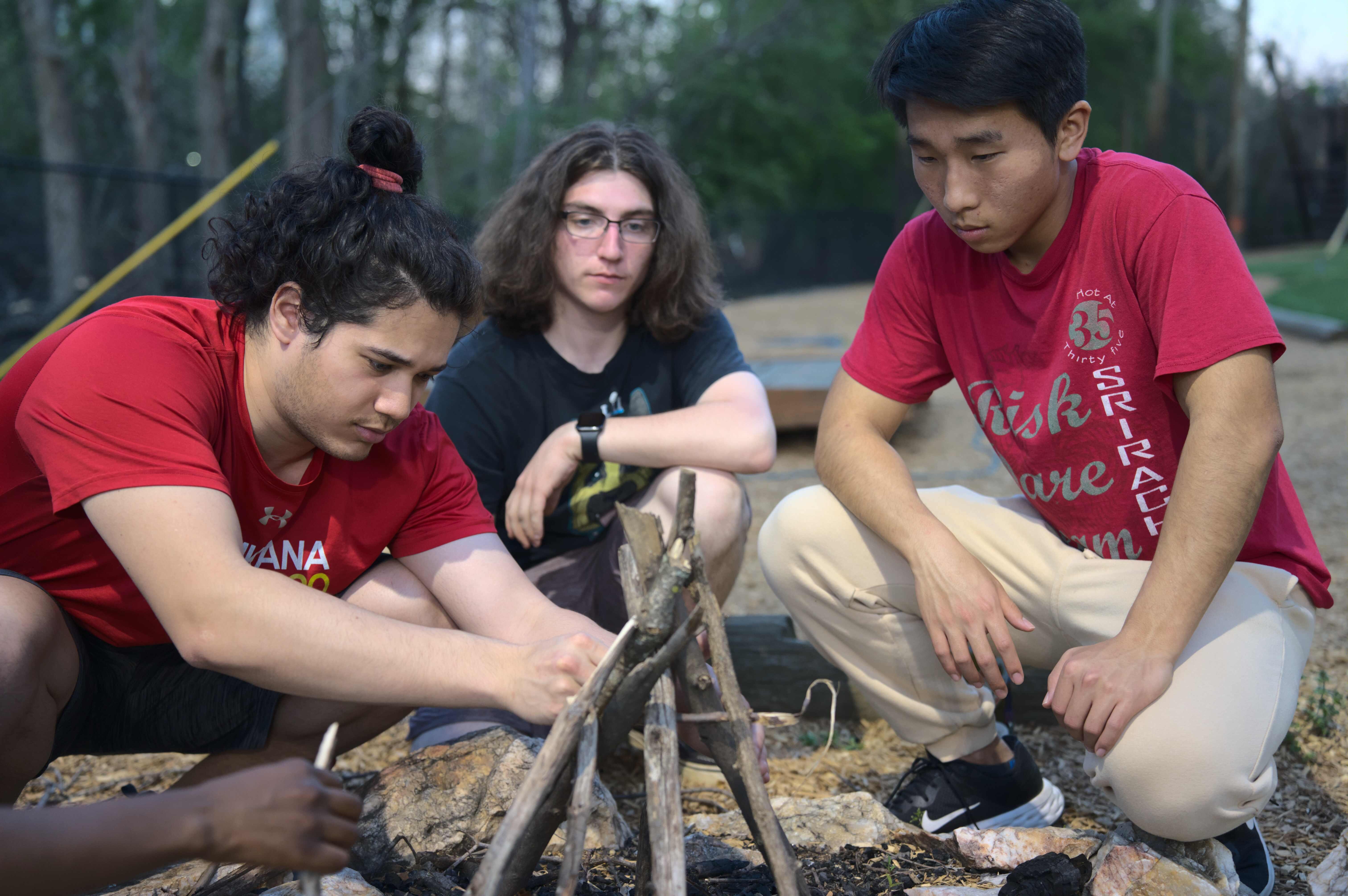 three students work on building a fire