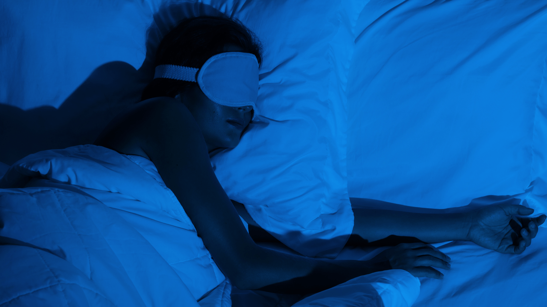 Woman sleeping in dark blue room with sleeping mask
