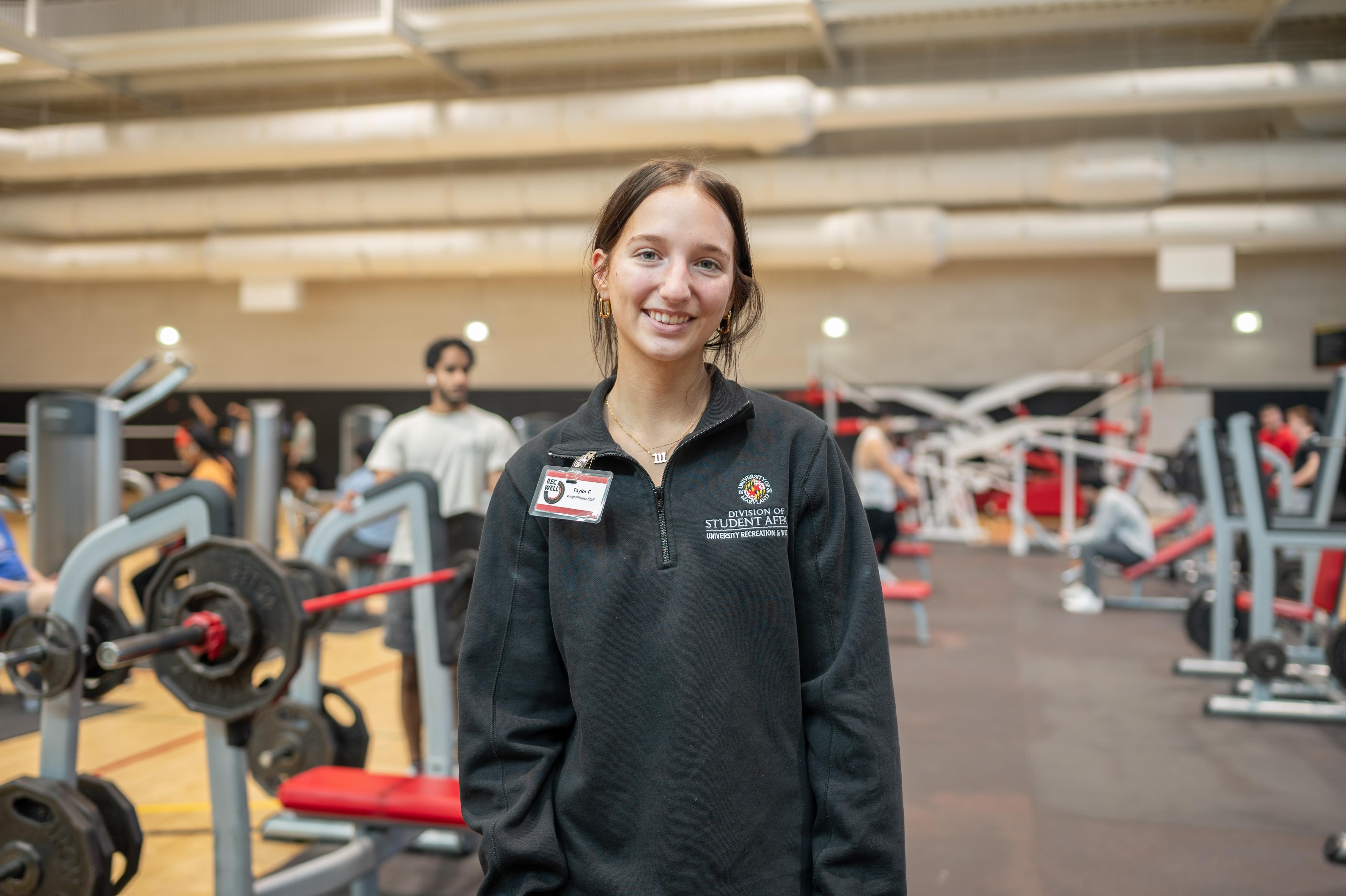 A Weight/Fitness Student Employee smiles for the camera in the East Gym weight room.