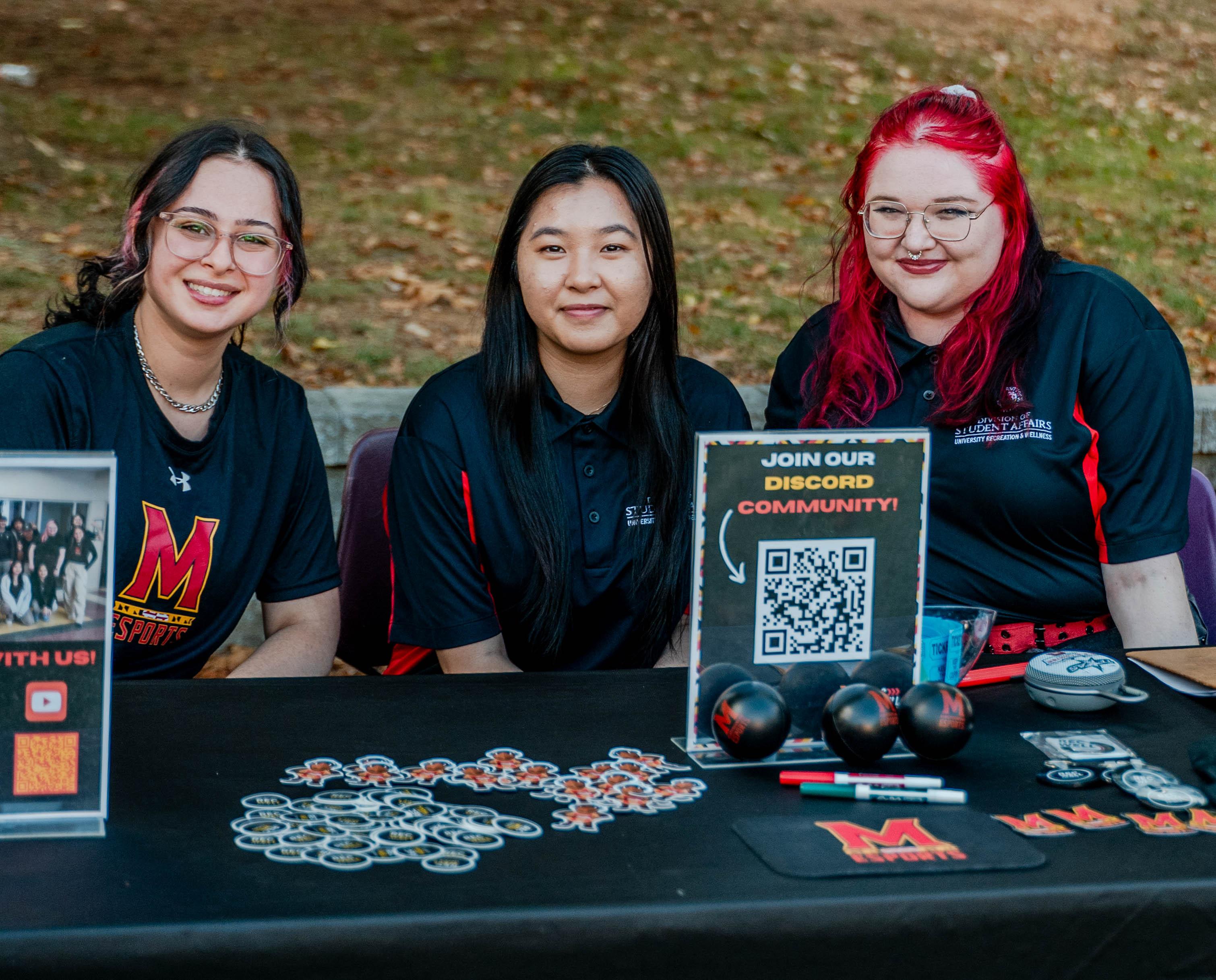 Three Terps Esports employees smile at camera, while tabling at an event.